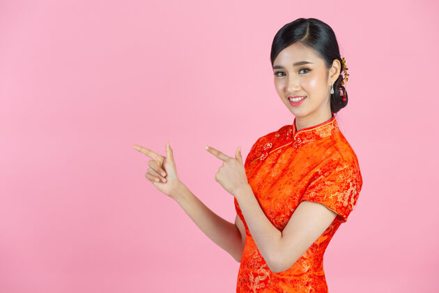 欢呼美丽的亚洲女人快乐的微笑 在中国新年的粉红色背景上向你展示一些东西衣服女人女孩