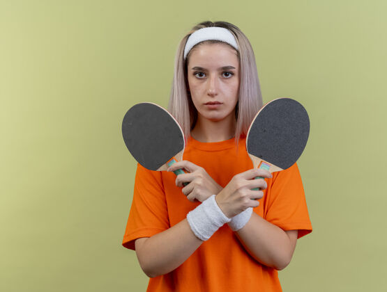 穿自信的年轻白人运动女孩戴着背带 戴着头带和腕带 手里拿着乒乓球拍腕带空间举行