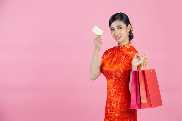 东方美丽的亚洲女人快乐的微笑和购物在中国新年的粉红色背景购物年轻女性