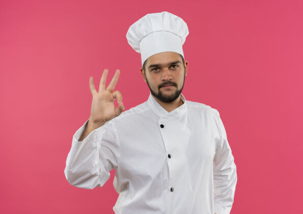 年轻自信的年轻男厨师身着厨师制服 在粉红色的墙上贴着“做得很好”的牌子厨师自信烹饪