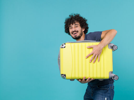 男度假的男人手里拿着大大的黄色手提箱 笑在蓝色上旅行人旅行