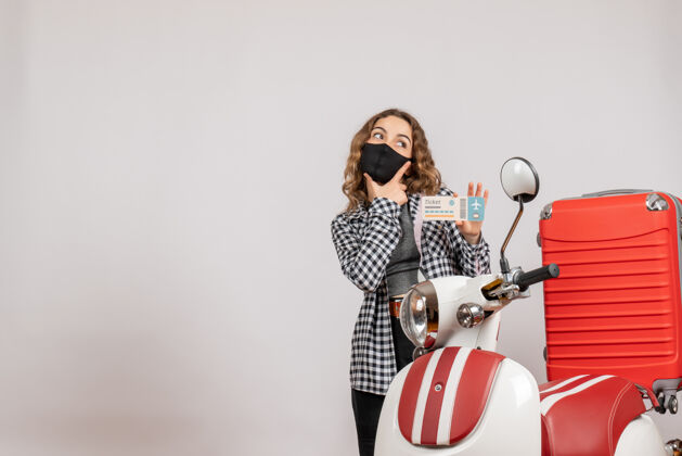 成人带着面具的体贴的年轻女孩站在带着手提箱的轻便摩托车旁边模特可爱手提箱