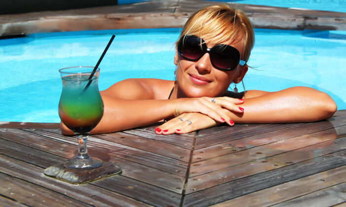 模特特写镜头中一个微笑的金发女性拿着果汁杯在游泳池里自然女人明亮