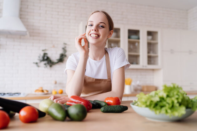 享受年轻漂亮的女人在厨房里围着围裙 桌上放着新鲜的蔬菜美丽欢呼成人