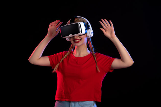成人年轻女性戴着耳机在黑暗的墙上玩虚拟现实的前视图视图耳机人物