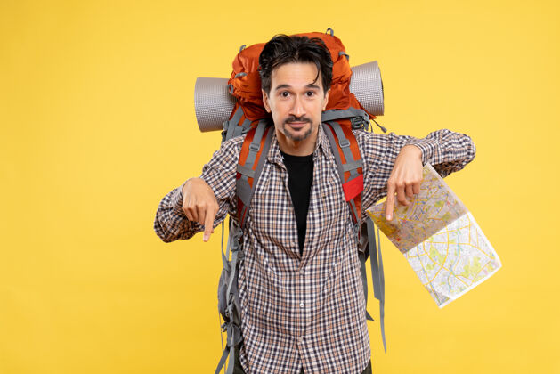 成人正面图：年轻男性带着背包徒步旅行 手持黄色背景的地图 公司旅行 空气 自然 校园 森林的颜色肖像徒步旅行校园