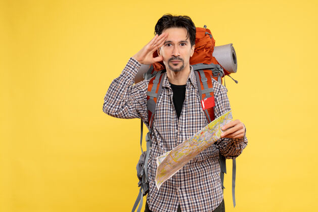 年轻男性正面图：年轻男性带着背包徒步旅行 手持黄色背景的地图 公司旅行 空气 自然森林的颜色人旅行音乐家