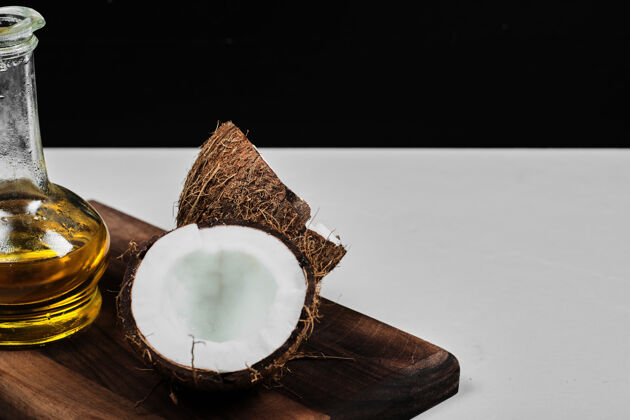 热带半切椰子和一瓶油放在木板上白色木材水果