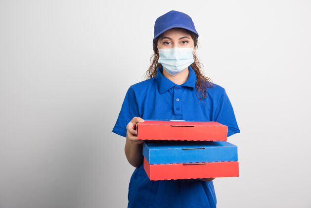面罩送比萨饼的女孩手里拿着三盒白色的医用面膜展示女性美味