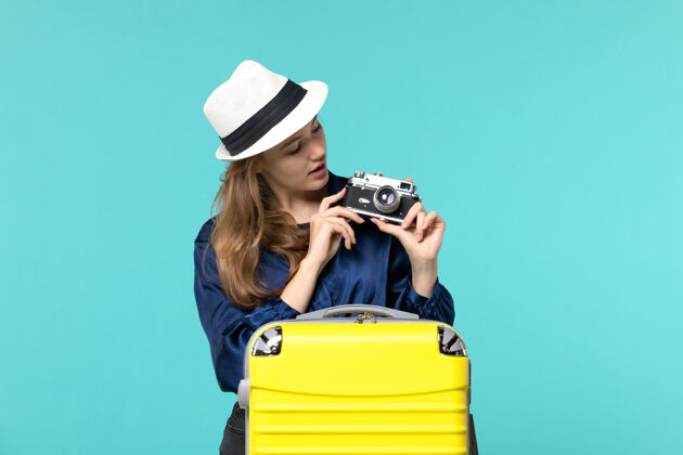 成人前视图年轻女子手持相机 在蓝色背景的女子海上旅行飞机上拍照女士摄影师旅行