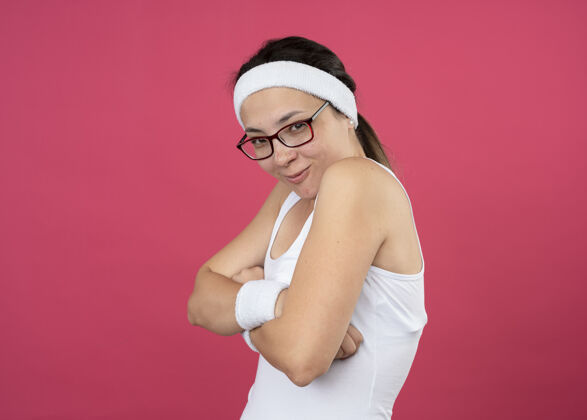 手臂戴着眼镜戴着头带和腕带的快乐的年轻运动女孩交叉双臂站在一边年轻复制眼镜