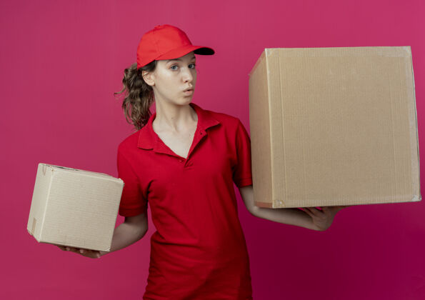 盒子令人印象深刻的年轻漂亮的送货女孩在红色制服和帽子举行纸箱看着深红色的空间深红色年轻漂亮
