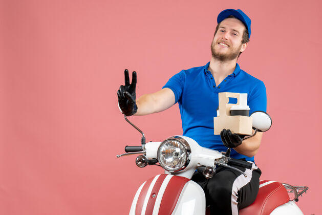 工作正面图穿着蓝色制服的男信使坐在自行车上 手里拿着粉红色的咖啡服务制服工作