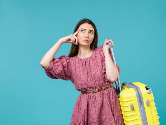 年轻的女人正面图年轻女子带着她的黄色袋子在蓝色背景上度假旅行夏日女人人类之旅海洋人包旅程