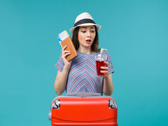旅程前景度假中的女人拿着果汁带着机票上蓝色背景的海上避暑女飞机旅行肖像航程女