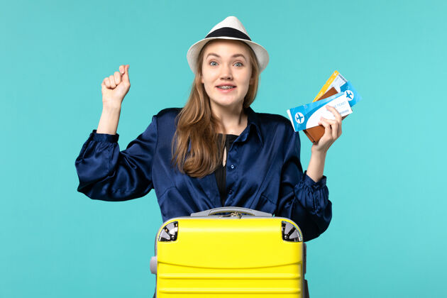 微笑正面图年轻女子拿着机票 正准备在蓝色背景的海上旅行飞机度假举行美丽票