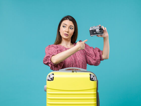 年轻女子正面图度假的年轻女子手持相机在蓝色背景下旅行海上旅行女子出国度假旅程微笑成人