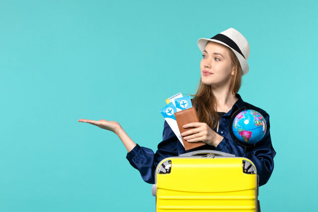 旅程前视图年轻女子手持机票和地球仪在淡蓝色背景飞机海上度假旅行浅蓝色肖像人