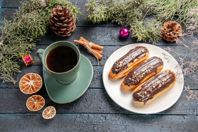 咖啡下图：白色椭圆形平板上的巧克力蛋糕 冷杉树枝和圆锥体 圣诞玩具 深色木桌上的一杯茶茶木头黑暗
