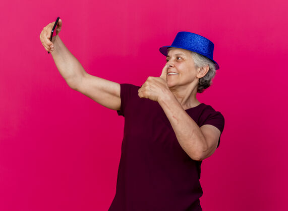 女人微笑着戴派对帽的老太太竖起大拇指 拿着粉色的手机看着老人电话拇指