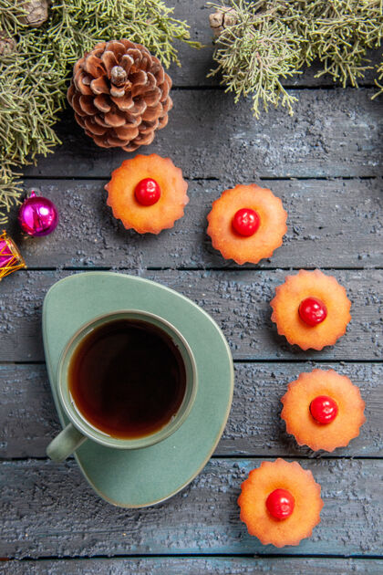 圣诞节顶视图圆形樱桃纸杯蛋糕杉树树枝圣诞玩具一个圆锥体和一杯茶在深色的木桌上顶部圆锥体热的