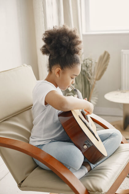 快乐卷发的小女孩学弹吉他坐在椅子上的小女孩教训有趣男人