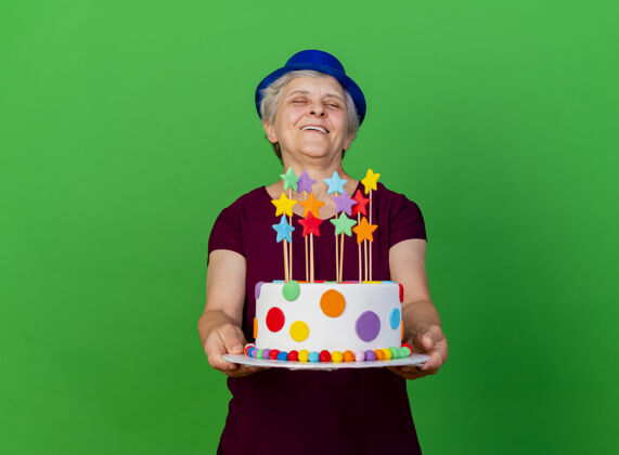 蛋糕戴着派对帽的快乐老太太在绿色的草地上拿着生日蛋糕女人欢乐老人