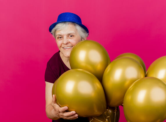 帽子微笑着戴着派对帽的老妇人手持粉色的氦气球站在那里站着粉色老人