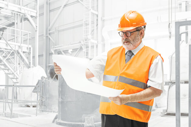 工人穿着建筑背心和橙色头盔的建筑工人站在白色的工作室墙上项目职业安全帽