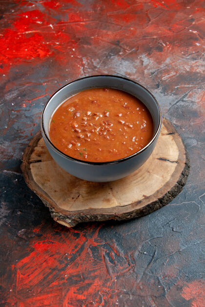 碗番茄汤在蓝色碗里的垂直视图 在一个棕色的木制托盘上 在混合颜色的桌子上托盘果汁番茄汤