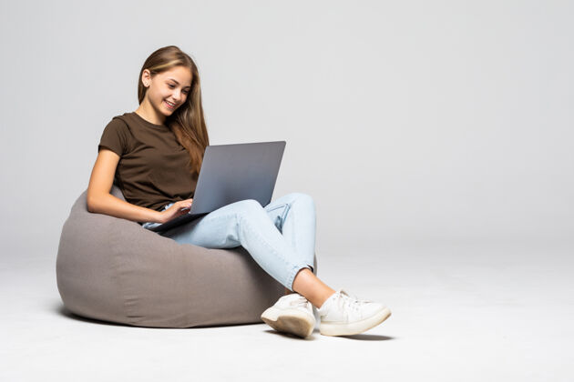 白色快乐的年轻女子坐在地板上用笔记本电脑在灰色的墙上年轻笔记本电脑女孩