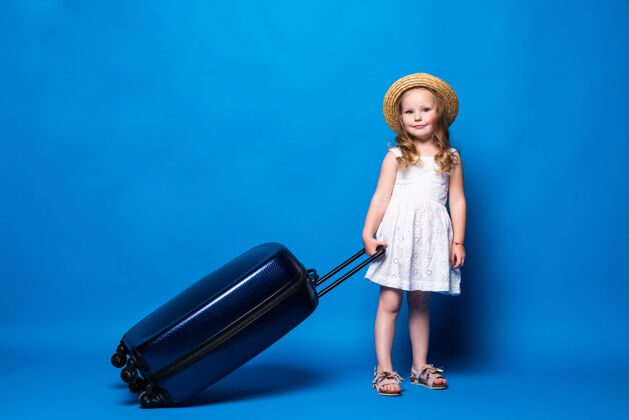 度假美丽的小女孩和行李隔离在蓝色墙上的全长肖像周末出国旅行的乘客航空旅行的概念旅游美丽游客