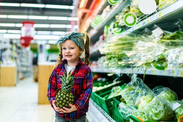 孩子可爱的小女孩拿着菠萝在食品店或超市快乐买购物