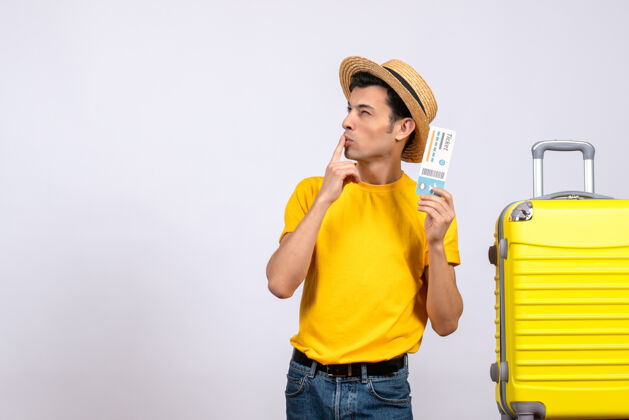 男正面图：年轻的游客站在黄色的手提箱旁想着什么成人呼叫男