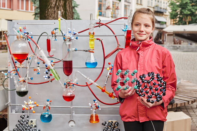 研究一个可爱的学龄女孩在一个化学过程的模型旁边摆姿势班级化学化学