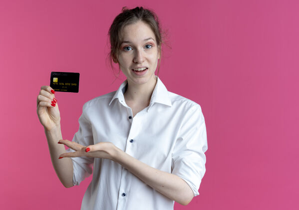 金发年轻的惊讶的金发俄罗斯女孩持有并指向信用卡惊喜持有女孩