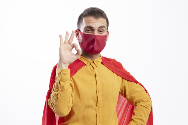 脸自信的超级英雄身穿红色斗篷 戴着红色面具 手势ok 手势孤立在白墙上表情超级英雄斗篷