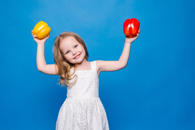 蔬菜美丽的小女孩抱着被隔离在蓝色墙上的甜椒蔬菜可爱女孩
