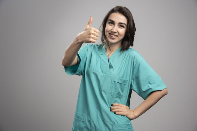 肖像女医生在灰色背景上竖起大拇指高质量照片检查医生工作