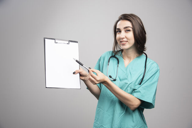 微笑女医生在灰色背景上展示剪贴板高质量照片疾病治疗女性