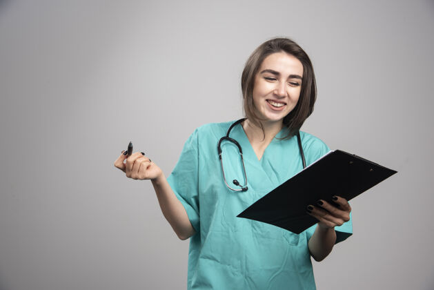 女性快乐的医生在灰色背景上看剪贴板高质量的照片健康医院检查