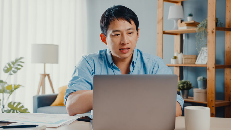 男人年轻的亚洲商人使用笔记本电脑和同事谈论视频通话计划 同时在家里智能工作流行病互联网年轻人