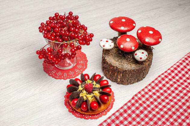 树桩俯视图红色葡萄干在一个水晶玻璃和浆果蛋糕上的红色椭圆形蕾丝doily和蘑菇的树桩上手工制作的白色木桌上餐桌木头水晶