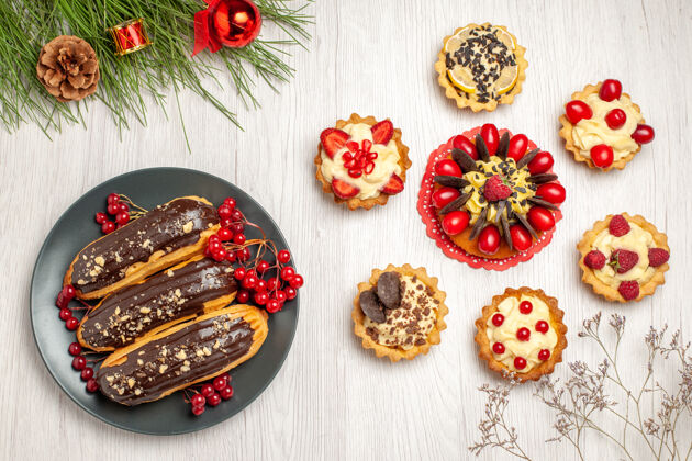 树俯瞰图：白色木质地面上 灰色的浆果蛋糕上放着巧克力和醋栗 圆形的馅饼和松树叶子 还有圣诞玩具圆晚餐肉