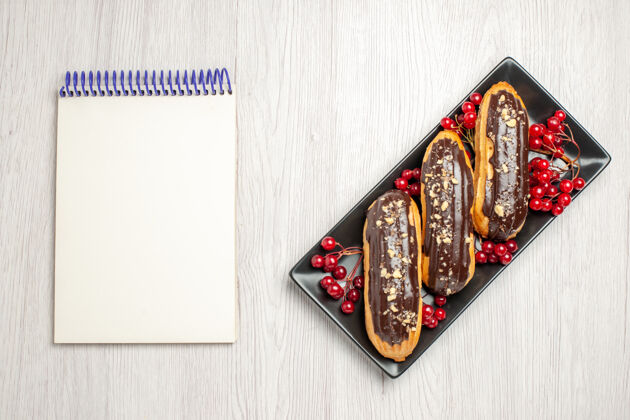 笔记本俯视图：右侧黑色等距矩形板上的巧克力和葡萄干 左侧白色木质地面上的笔记本壁板木头铅笔盒