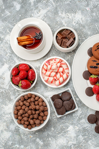 食物俯瞰饼干草莓和圆形巧克力放在椭圆形的盘子里 糖果草莓巧克力麦片和桂皮茴香茶放在灰白色的桌子上巧克力碗水果