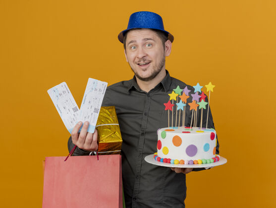 票高兴的年轻人戴着蓝色的帽子拿着蛋糕和礼物和门票孤立的橙色请拿着年轻人