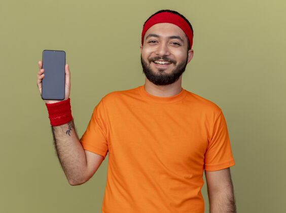 男士微笑着的年轻人戴着头带和腕带 手拿着橄榄绿的手机腕带年轻电话