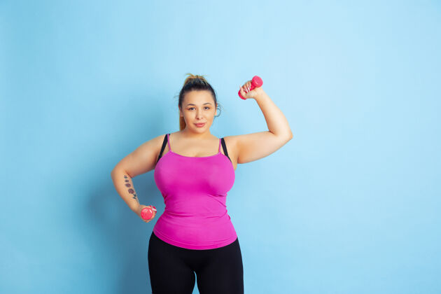 积极年轻的白人大号女模特在蓝色背景下的训练运动概念 人类的情感 表达 健康的生活方式 身体积极 平等重量训练 复制空间训练饮食十字架