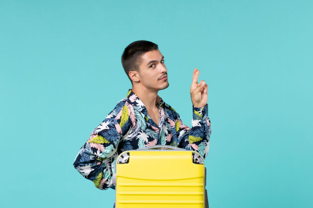 书桌正前方的年轻男性准备旅行与他的黄色袋子在蓝色的表面度假快乐年轻男性